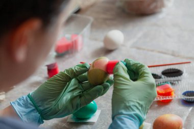 Plastik mavi eldivenli eller paskalya yumurtalarını sıvı boyalarla boyayarak bulaşık yıkama çubuğu kullanıyorlar.