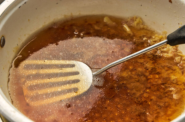 Old dirty greasy pan with a spatula closeup. Droplets of oil mixed with water and leftovers after food preparation