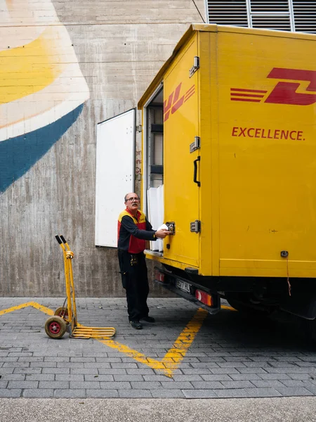 Descarga do trabalhador sênior pacotes DHL de caminhão na praça central — Fotografia de Stock