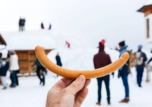 Sausage in hand with silhouettes of people in background — Stock Photo, Image