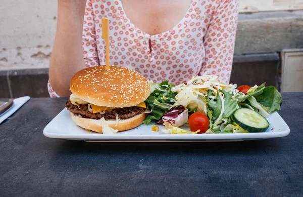 Woman eating delicious salad with tasty burger — Stock Photo, Image