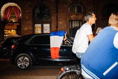 STRASBOURG, FRANCE - JULY 10, 2018: Woman waving French flag from passing car celebration after the victory of France qualify for the final of the 2018 FIFA World Cup after their victory clipart