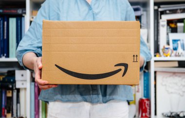 Paris, Fransa - 4 Temmuz 2018: kadın unboxing, gururlu Amazon Prime istemci arka planda kitaplığıyla yapmaya hazırlanıyor teslim Amazon Prime paket alma