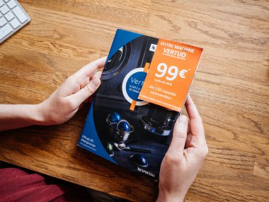 Paris, Fransa - 1 Temmuz 2018: kadın ahşap ofis okuma tablo bir reklam broşür katalog Nespresso espresso makineleri demlemek espresso kahve kahve kapsül makineleri için ev ile veya