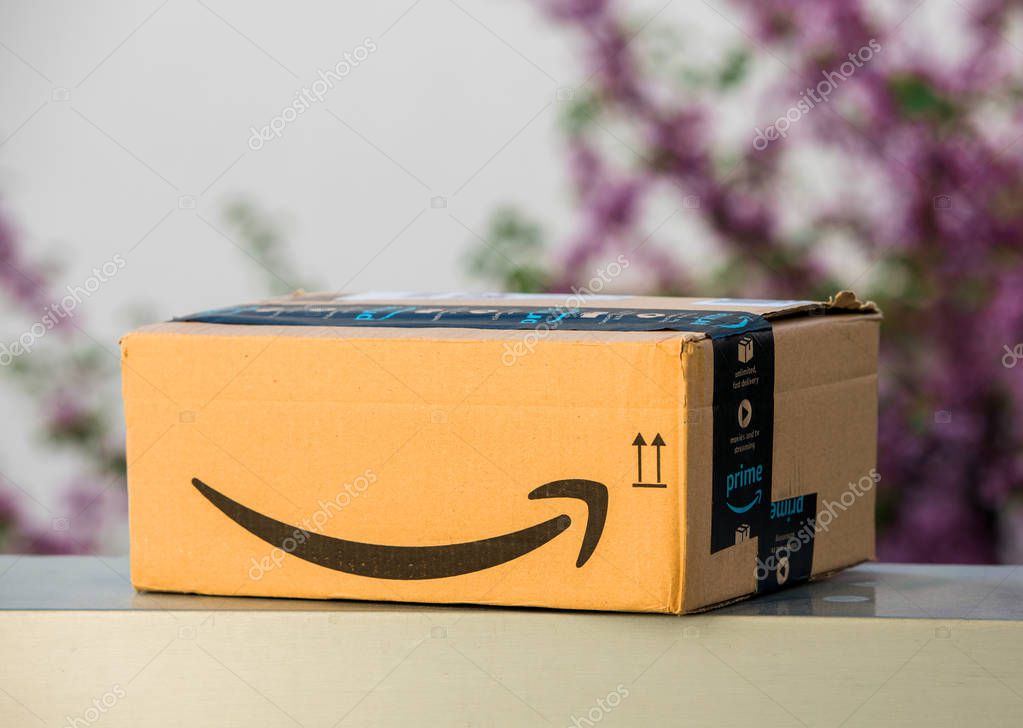 PARIS, FRANCE - APR 19, 2018: Delivered Amazon Cardboard box left outdoor the house by courier with large Amazon Smile logotype against defocused tree background