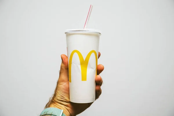 PARIS, FRANCE - JUL 27, 2018: Man holding against white background a cup of McDonalds Cola with plastic straw with yellow logo near one of the worlds largest fast food restaurants — Stock Image Paris France Jul 2018 Man Holding White Background Cup Mcdonalds Stock Picture