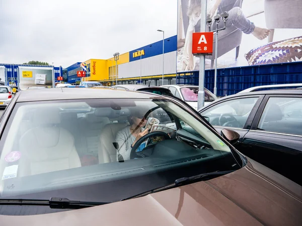 DELFT, NETHERLANDS - AUG 23, 2018: View from street of elegant woman reading IKEA furniture magazine catalog inside car parked on the IKEA parking in the main store in netherlands, headquarter of IKEA — Stock Image Delft Netherlands Aug 2018 View Street Elegant Woman Reading Ikea Stock Picture
