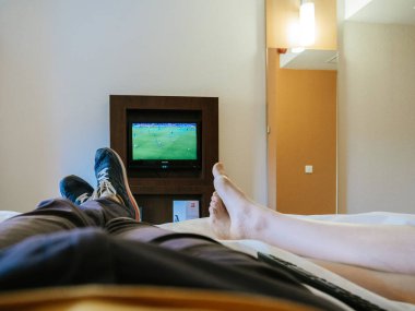 Barcelona, İspanya - 3 Haziran 2018: Kırpma atış erkek ve kadın yatakta otelde soğutma ve Ibis otel TV'de futbol izlerken bacak