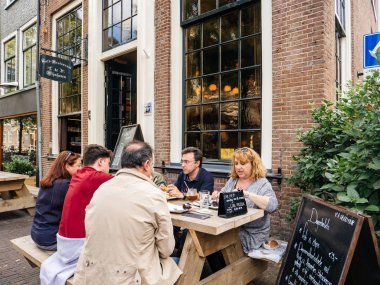 Texel, Hollanda - 19 Ağustos 2018: Grup arkadaşıyla terasta açık havada, kafeterya Hollanda Texel Adası cityscape cadde görünümü üzerinde masada yemek yiyor olması 