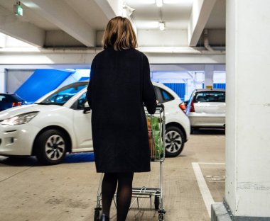 Elinde çanta bakkaliye otopark ile otopark için alışveriş arabası itme kadın arkadan görünüş
