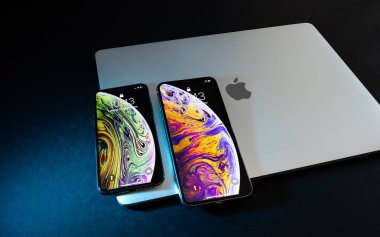 PARIS, FRANCE - SEP 25, 2018: Two new iPhone Xs and Xs Max smartphone model by Apple Computers close up on laptop MacBook pro closed lid. Newest golden Apple iPhone 11 mobile phone device  clipart