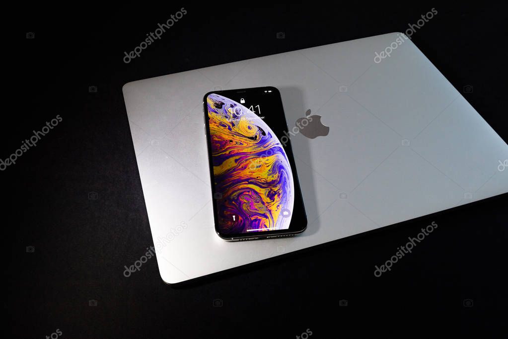 PARIS, FRANCE - SEP 25, 2018: New latest iPhone Xs smartphone model by Apple Computers close up on closed lid of a MacBook pro laptop with home apps on OLED displays