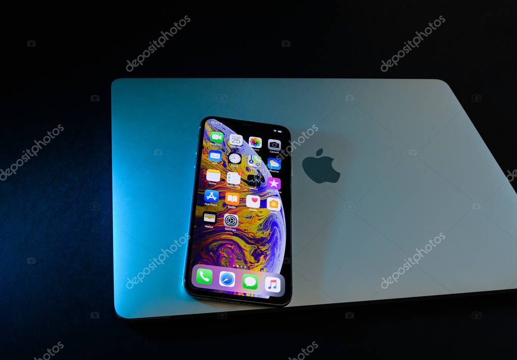 PARIS, FRANCE - SEP 25, 2018: New latest iPhone Xs smartphone model by Apple Computers close up on closed lid of a MacBook pro laptop with home apps on OLED displays - blue light