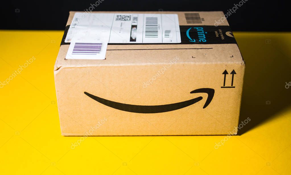 PARIS, FRANCE - SEP 28, 2018: Small Amazon parcel cardboard box against yellow background smile logo. Amazon Prime is the online paid subscription service offered by Amazon.com web-commerce site