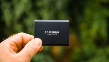 PARIS, FRANCE - AUG 14, 2018: Man hand presenting holding Samsung T5 Portable SSD 2 tb external hard drive disk with high read and write speed against green background unboxing testing  clipart