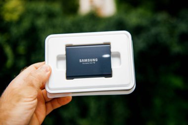 Paris, Fransa - 14 Ağustos 2018: Adam elini tutarak plastik kutu Samsung T5 taşınabilir Ssd 2 tb harici sabit disk disk yüksek okumak ve yazmak hız karşı yeşil arka plan unboxing test ile 