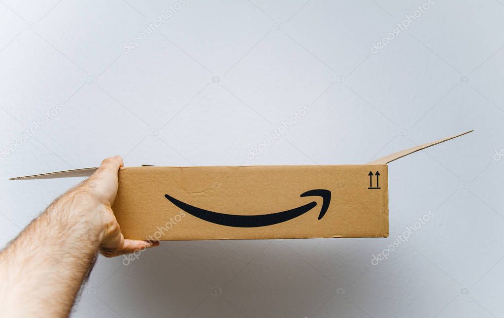 PARIS, FRANCE - AUG 11, 2018: Man holding against white background freshly unboxed Amazon Prime cardboard box
