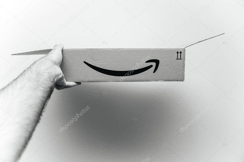 PARIS, FRANCE - AUG 11, 2018: Man holding against white background Amazon Prime cardboard box after the unboxing showing the open box - black and white