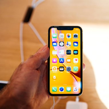 STRASBOURG, FRANCE - OCT 26, 2018: Customer POV holding new yellow iPhone XR smartphone next to white one in Apple Store Computers during the launch day home screen with all apps 