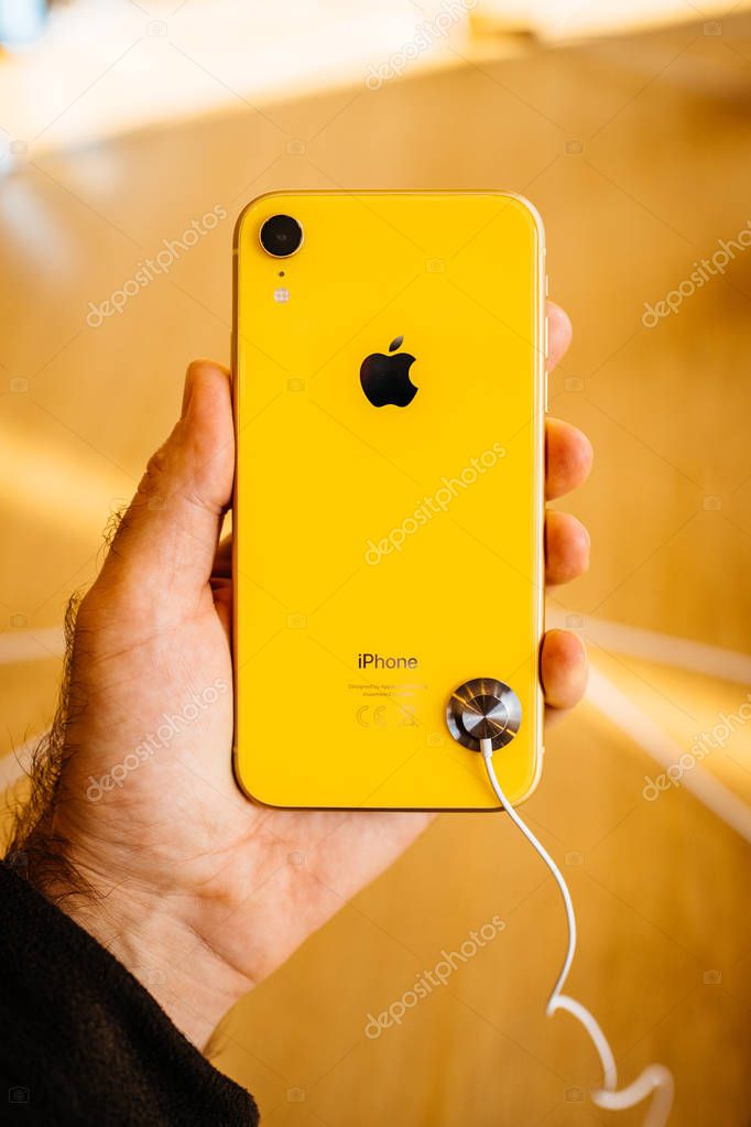 STRASBOURG, FRANCE - OCT 26, 2018: Customer holding admiring testing latest yellow iPhone XR smartphone in Apple Store Computers during the launch day woth Apple logo steel case