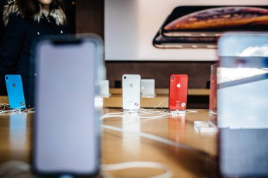 PARIS, FRANCE - OCT 26, 2018: Latest iPhone XR smartphone in Apple Store Computers during the launch day- view of red phone in docking station clipart