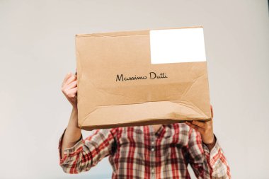 Woman hiding behind cardboard from Massimo Dutti fashion label o clipart