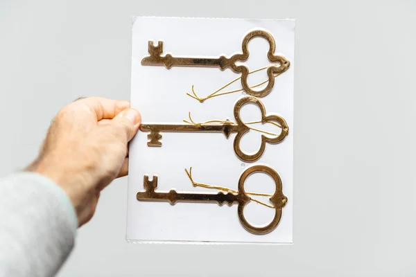 Homem segurando três novas chaves douradas fundo branco — Fotografia de Stock