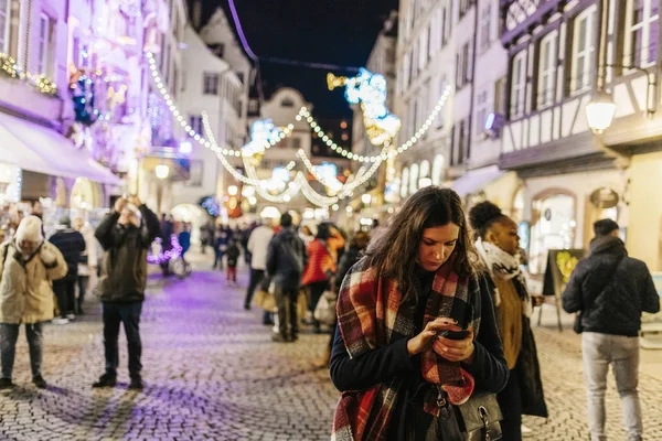 Frau benutzt Smartphone auf Straßburger Weihnachtsmarkt in der Abenddämmerung — Stockfoto