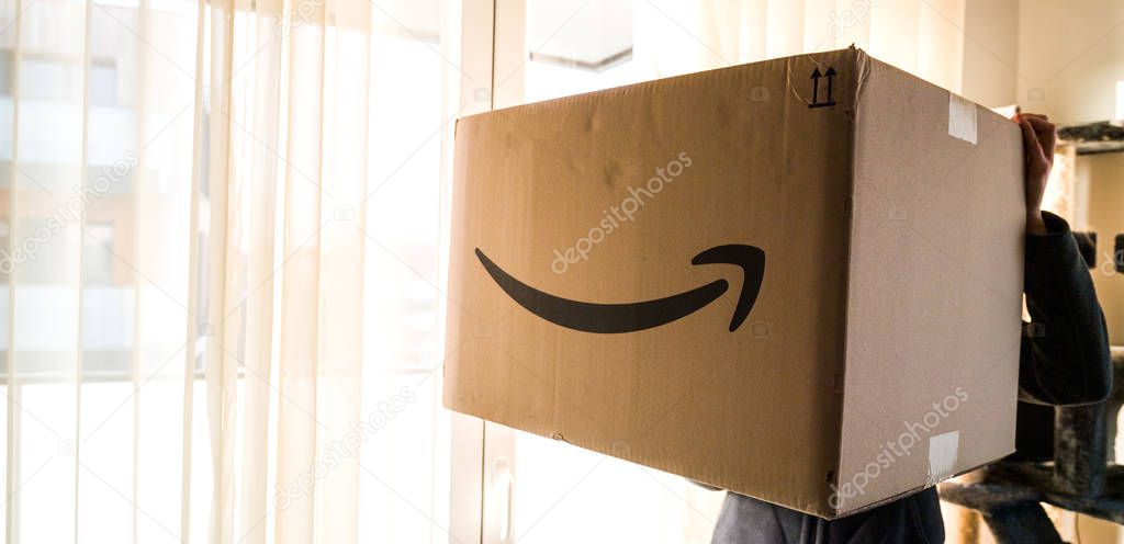 PARIS, FRANCE - DEC 25, 2018: Wide image of woman holding large Amazon Prime parcel cardboard box on Christmas day with big huge gift inside