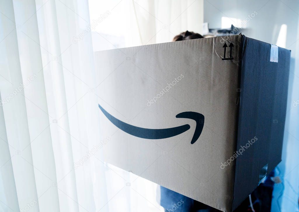 PARIS, FRANCE - DEC 25, 2018: Blue toned image of woman holding large Amazon Prime parcel cardboard box on Christmas day with big huge gift inside