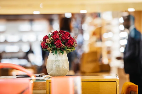 Rosas rojas en un jarrón de cerámica con silueta de vendedor y clientes — Foto de Stock