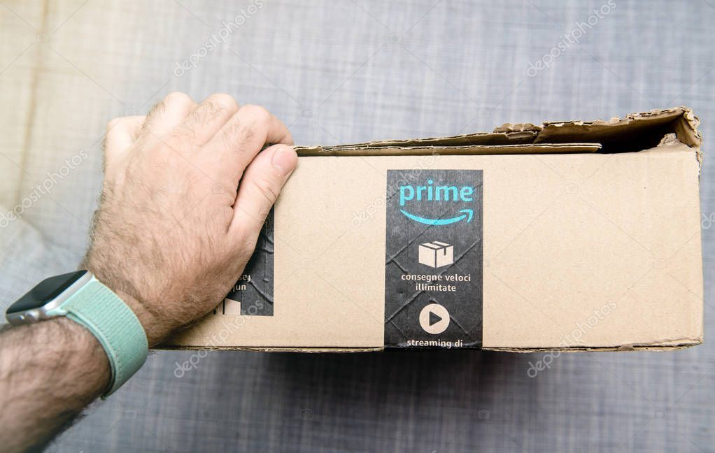 Paris, France - Jun 11, 2018: Man holding hand on cardboard box with Amazon Prime logotype and scotch tape fast delivery e-commerce parcel