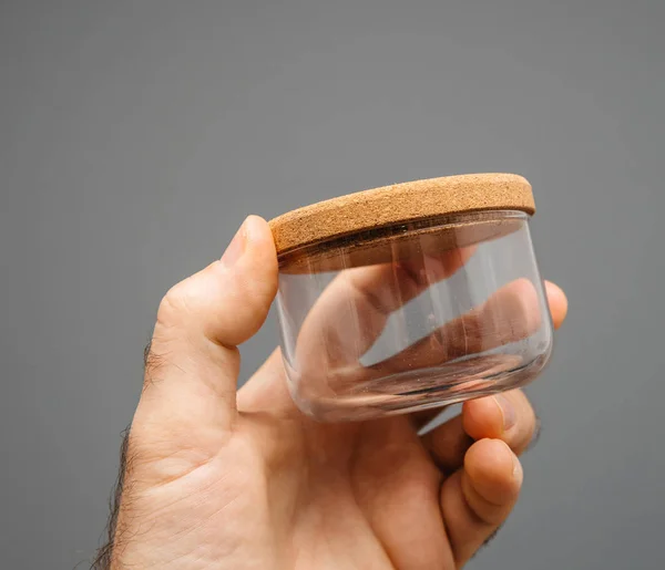 Glasgefäß mit Korkdeckel in männlicher Hand grauer Hintergrund — Stockfoto