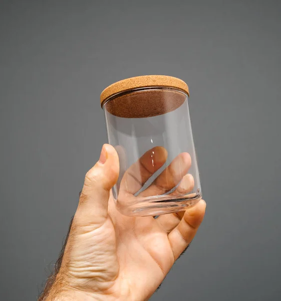 Tarro de vidrio con tapa de corcho en fondo gris mano macho — Foto de Stock