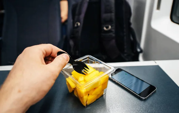 Man eating fruit salad with fork in train