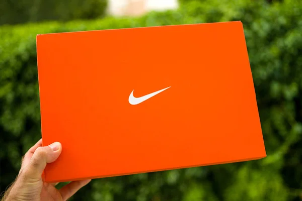 Mano del hombre sosteniendo la nueva caja de cartón Nike contra el parque verde —  Fotos de Stock