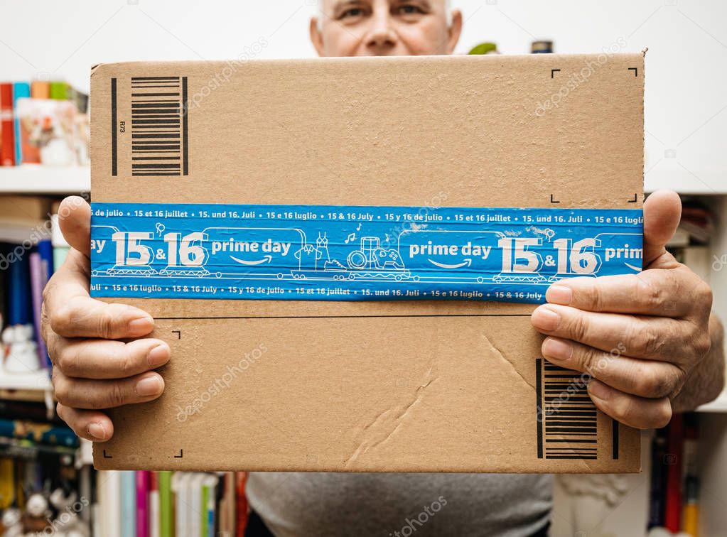 PARIS, FRANCE - JUL 12, 2108: Senior man holding Amazon Prime Day cardboard parcel with special blue scotch tape for the Prime Day offering a day of deals, discounts, and unabashed shopping