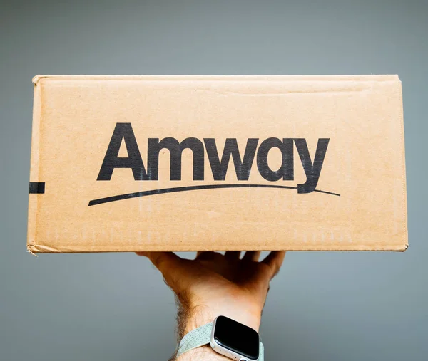 Paris, Frankreich - 2. Juli 2019: Mann hält Geschenk vor grauem Hintergrund Pappschachtel mit amway Schriftzug — Stockbild Mann hält Paket in der Hand — Stockfoto