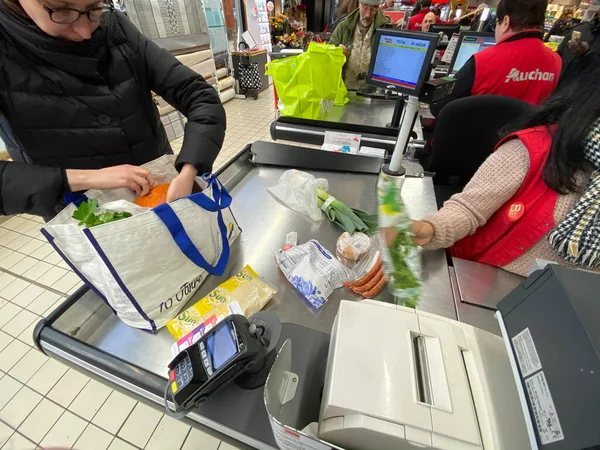 Mujer en el embalaje en su bolsa de múltiples productos comprados en el supermercado Auchan francés — Foto de Stock