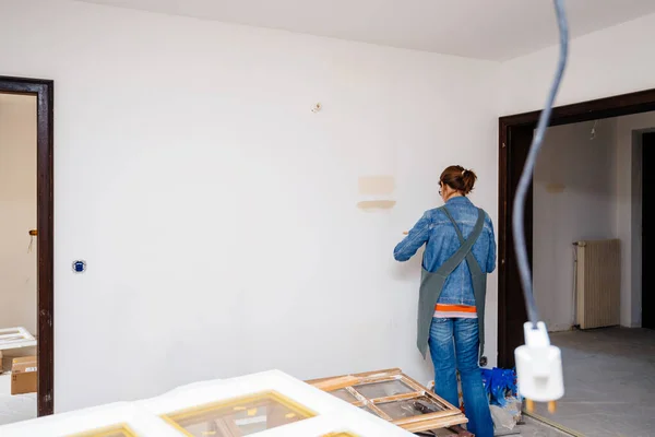 Vista lateral da mulher arquiteta testando pintura leve na parede da sala renovada — Fotografia de Stock