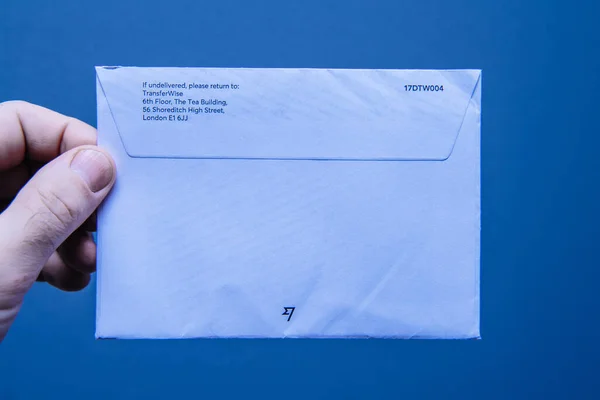 TransferWiseのアドレスを持つ青の背景紙の封筒を保持 — ストック写真