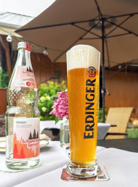 Trier, Almanya - 5 Temmuz 2025: Schwarzwald Sprudel 'in yanındaki teras masasında köpüklü uzun Erdinger bira bardağı şemsiyenin altında..