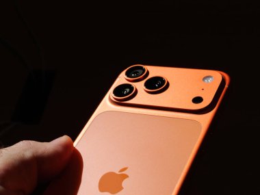 Paris, Fransa - Sep 19, 2025: Apple iPhone 17 Pro Max 'i turuncu renkte tutan bir erkeğin yakın çekimi, üçlü kamera sistemini ve parlak metalik tasarımı vurguluyor.