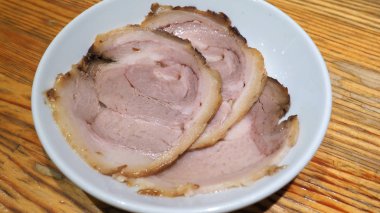 Chashu domuz eti 3 adet dilim beyaz renk çanak ve ahşap masa Tepesi tonkotsu ramen Sapporo Hokkaido Japonya'deki ünlü geleneksel gıda için hangi ek menü.