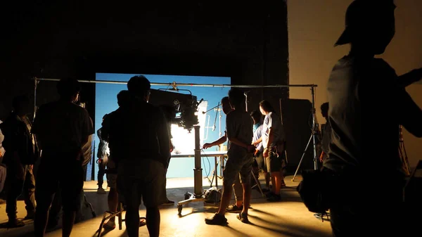 幕后的视频制作拍摄工作室的剪影 有专业的设备 如相机 三脚架和蓝屏背景设置的色度关键技术在后处理和许多电影船员团队工作的电视广告或 — 图库照片