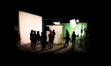 Silhouette images of video production behind the scenes or b-roll or making of TV commercial movie that film crew team lightman and cameraman working together with director in big studio with professional equipments  clipart