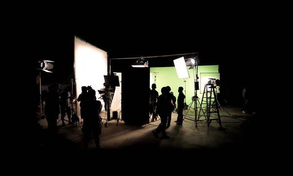 その映画の乗組員チーム ライトマンとカメラマンのプロ機器との大きなスタジオのディレクターとの連携シーンや ロールの後ろにビデオ制作のシルエット画像やテレビの商業映画のメイキング — ストック写真