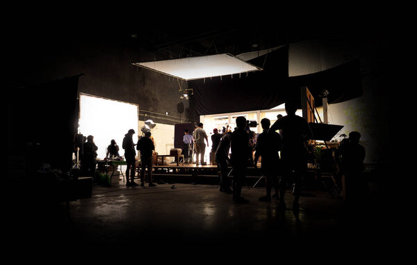 Низкий ключ силуэт освещения производства VDO за кулисами, которые съемочная группа настраивает камеру и устанавливает для съемок и ожидания режиссера нормально со сценами в мониторе
.