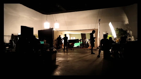 Behind the shooting video production and lighting set for filming which movie crew team working and silhouette shadow of camera and professional equipment in big studio for commercial advertising.