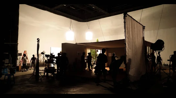 Behind the shooting video production and lighting set for filming which movie crew team working and silhouette shadow of camera and professional equipment in big studio for commercial advertising. — Stock Photo, Image